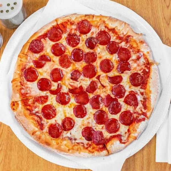 A whole pepperoni pizza with melted cheese on a white paper-lined tray on a wooden table.