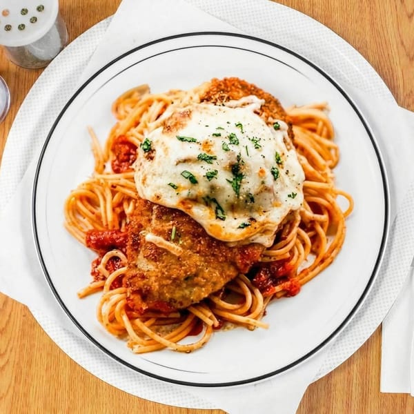 Chicken parmesan with melted cheese and fresh herbs, served over spaghetti with red sauce.