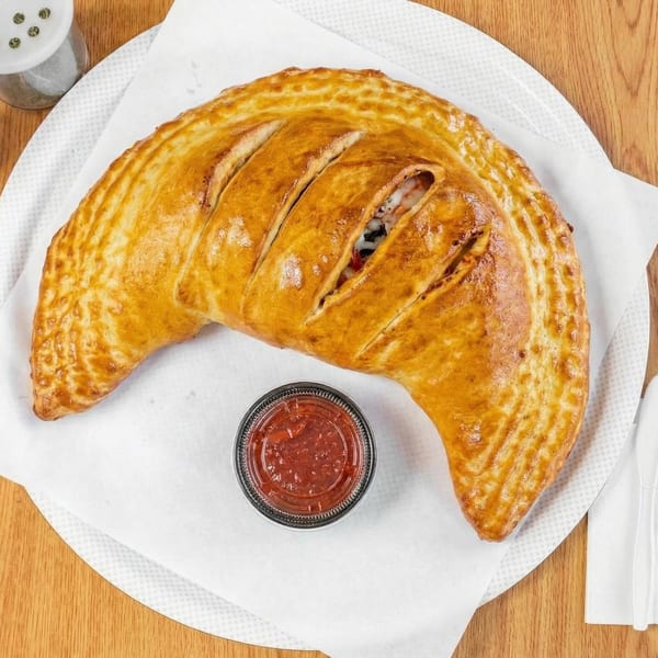 Golden-brown calzone with visible filling and a side of red marinara sauce on a white plate.