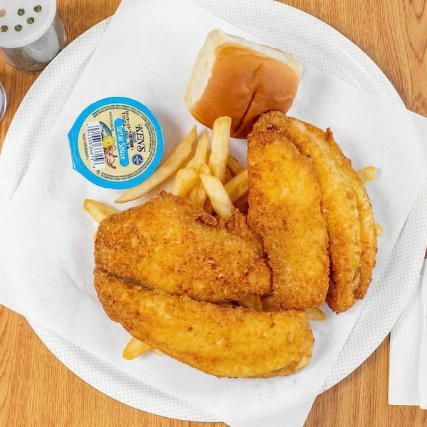 Fried fish fillets, french fries, a dinner roll, and a cup of tartar sauce on a white plate.