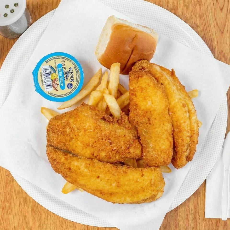 Fried fish fillets, french fries, a bread roll, and tartar sauce on a white paper-lined plate.