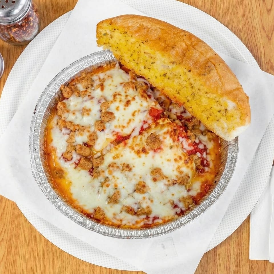 Baked ziti with melted cheese and sausage in a foil pan, served with a side of garlic bread.